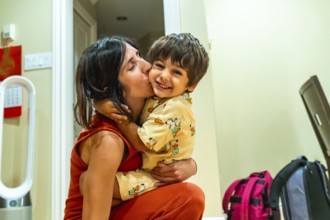 Happy mother kissing her cheerful son on the cheek while holding him in her arms, enjoying a warm