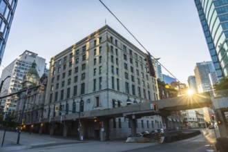 Sun is rising behind waterfront station, casting warm glow on historic building and modern