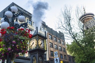 Gastown steam clock releasing clouds of steam amidst vibrant flowers, with the iconic harbour