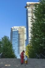 Mother and son climbing stairs together, surrounded by towering skyscrapers and lush trees in