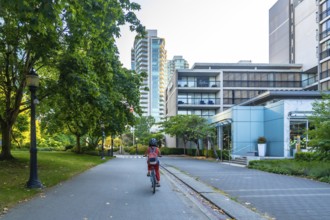 Woman with backpack and helmet is riding a bicycle on a paved path through a green park, passing by