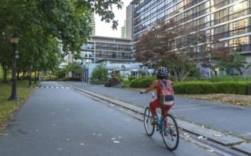 Woman with backpack and helmet is riding a bicycle on a dedicated bike lane next to a park,