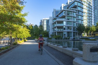 Woman wearing a helmet and backpack cycling on a paved path in an urban park surrounded by green