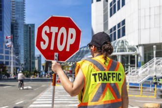 Traffic guard wearing high visibility vest holding stop sign regulating traffic flow on a city