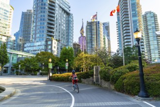 Student wearing a helmet and backpack cycling on a bike lane in downtown vancouver, surrounded by