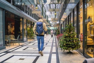 Person walking through a festively decorated shopping center with glass roof, Calwer Passage,