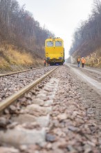 Yellow work train runs on a railroad track with workers on the line, stuffing machine on Hermann,