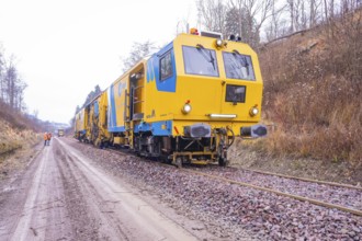 Yellow working trains on railroad tracks in a wintry landscape with gravel, stuffing machine on