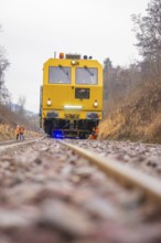 Yellow work machine on railroad track in autumn environment with workers, stuffing machine on