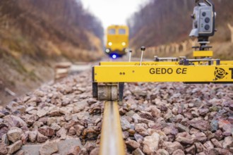 A Gedo CE device on rails with a yellow vehicle in the background, tamping machine on Hermann,