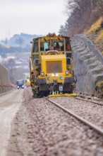 Yellow machine on rails during construction, with another vehicle in the background, tamping