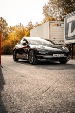 Black car on a road in a sunny autumn landscape, Deer e-Carsharing, Tesla Model 3, Calw, Germany