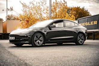 Elegant black car on a road with autumn trees in the background, Deer E-Carsharing, Tesla Model 3,