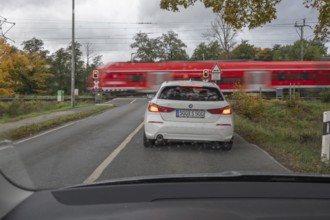 Regional train crosses a restricted level crossing, cars waiting in front of it, Fürth