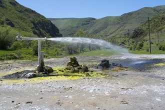 Natural spring with sparkling water jet against green mountain landscape under blue sky, Vardzia,