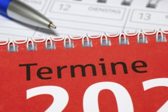 Close-up of red spiral calendar with blue pen, appointment calendar