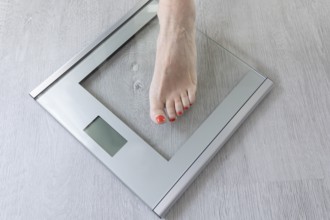 Foot of a woman standing on a digital bathroom scale while monitoring her weight. This scene