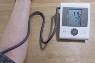 A woman sits relaxed at the table and independently measures her blood pressure with a blood
