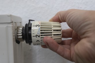 A hand grabs the thermostat head of a radiator to adjust the temperature. This image symbolizes