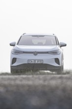 A white car seen from the front in a morning haze in an open landscape, VW ID4 electric car, Deer