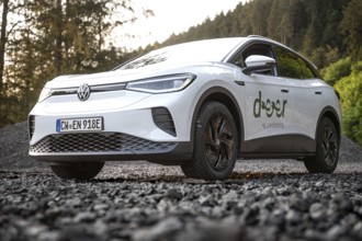 White car parked on gravel in forest in sunlight surrounded by trees, sense of adventure, VW ID4