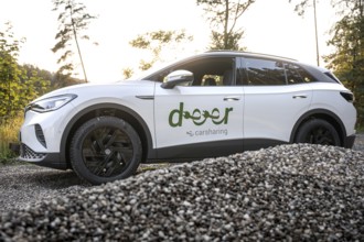 A white car stands on gravel against a forest backdrop at sunset, VW ID4 electric car, deer car