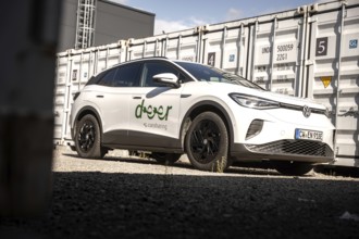 White car parked next to large grey containers under a blue sky in an urban environment, VW ID4