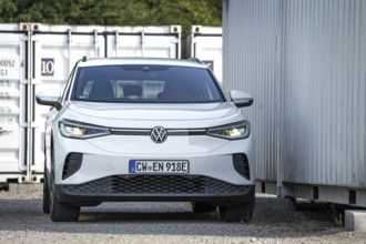 A white car parks between industrial containers and buildings, VW ID4 electric car, Deer