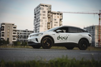 A white car is parked on a street with modern buildings in the background, VW ID4 electric car,