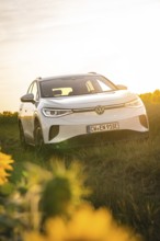 A white car in a meadow next to sunflowers at sunset, VW ID4 electric car, Deer Carsharing, Calw,