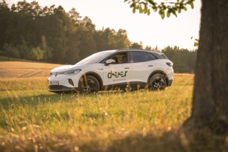 A white car in a meadow at sunset against a wooded background, VW ID4 electric car, deer car