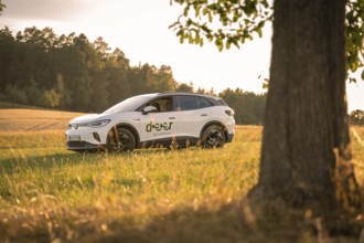 White car at sunset in a field, a tree in the foreground, rural atmosphere, VW ID4 electric car,