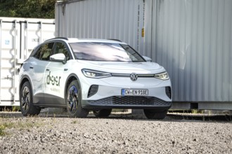 White car parked in a rocky place next to large metal containers, modern ambiance, VW ID4 electric