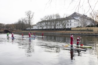 Water sports enthusiasts dressed up as Santa Claus ride SUPs on the Spree in front of Bellevue
