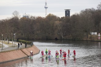 Water sports enthusiasts dressed up as Santa Claus ride SUPs on the Spree am Park at the