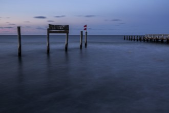 Wooden sign in the sea with inscription Zingst and wooden walkway, long exposure, evening light,