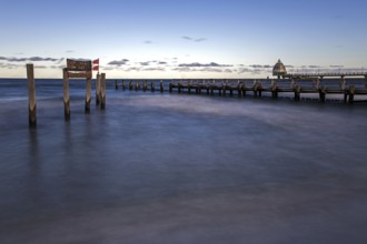 Wooden sign in the sea with inscription Zingst and wooden walkway, pier with diving gondola behind,