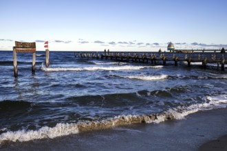 Wooden sign in the sea with inscription Zingst and wooden footbridge, back pier with diving