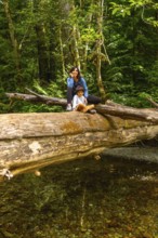 Mother and son sharing a peaceful moment on a large fallen log over a clear stream in the serene