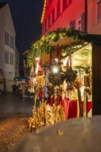 Sales stand at the Christmas market with wooden decorations and lights in the rain at night,