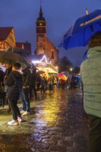 People with umbrellas on a wet Christmas market at night with illuminated church in the background,