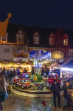 Families in front of an illuminated carousel with toys at a night-time Christmas market, Böblingen