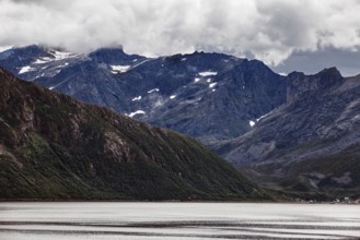 Impressive mountain landscape with snow-capped peaks and a quiet fjord under thick clouds, Norway