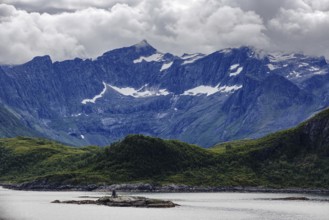Dramatic mountain range with snowy peaks and a fjord, under a cloudy sky, Norway