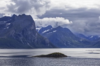 Unique view of rugged mountains and a small island in a quiet fjord under a cloudy sky, Norway