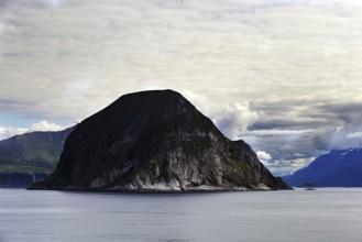 Barren rocky island surrounded by calm sea and cloudy sky, Norway