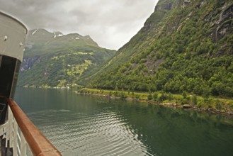 Scenic view of a fjord with forested mountains in the background and a ship in the foreground,