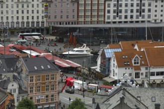 A lively marketplace with boats and surrounding historic buildings, mountains
