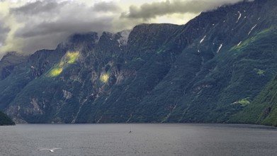Dramatic fjord under low-hanging clouds surrounded by steep, green mountains, Norway