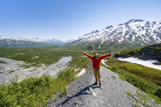 Hiker stretches his arms in the air, on the glacial moraine, view over the wide valley of the Tsina